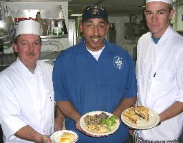 Mess Specialist Rahmel Leake (centre), here with Tim Richardson (left) and Ricky Wallenburg of Perth’s Rendezvous Observation City Hotel, shows a lunch meal onboard USS Shiloh.